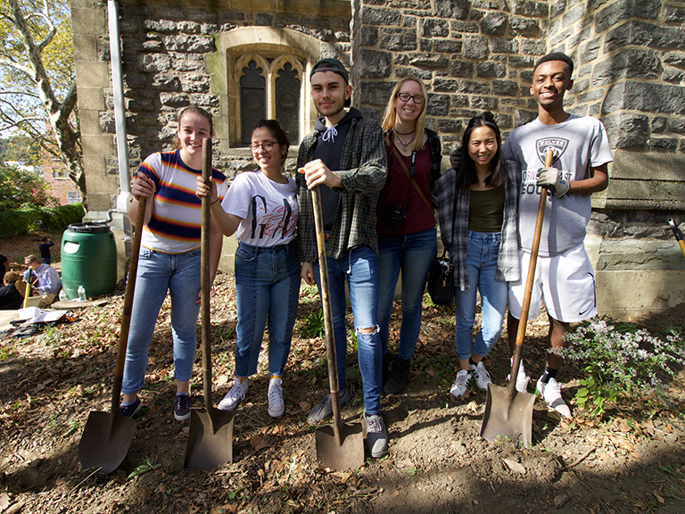 Students stand in park posing with shovels.