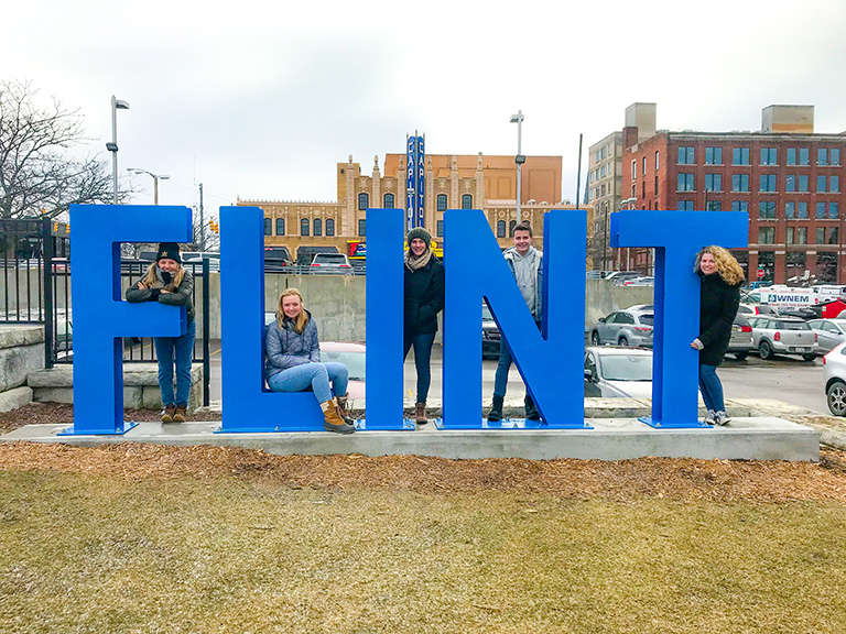 students standing behind flint sign in grass