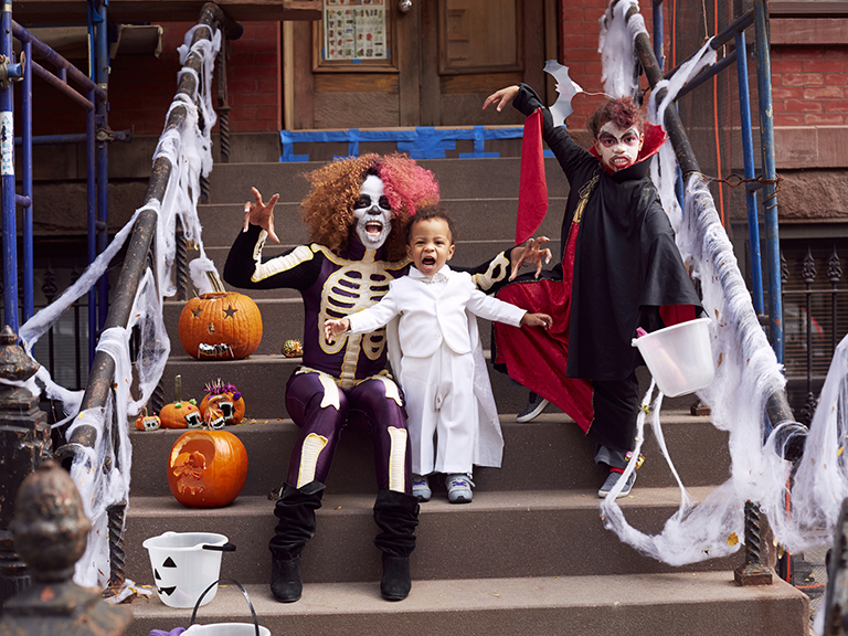 woman with halloween makeup stands with boy in white outfit on stoop in halloween costumes