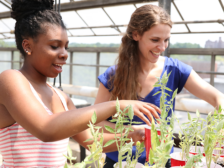An image of female professor and student looking at plants in greenhouse
